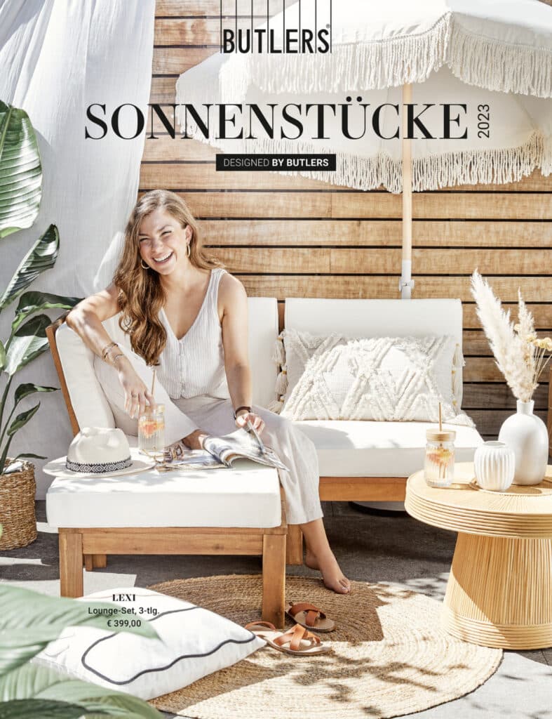 BUTLERS catalogus cover met een lachende vrouw in lichte kleding, zittend op een tuinbank en genietend van een drankje.