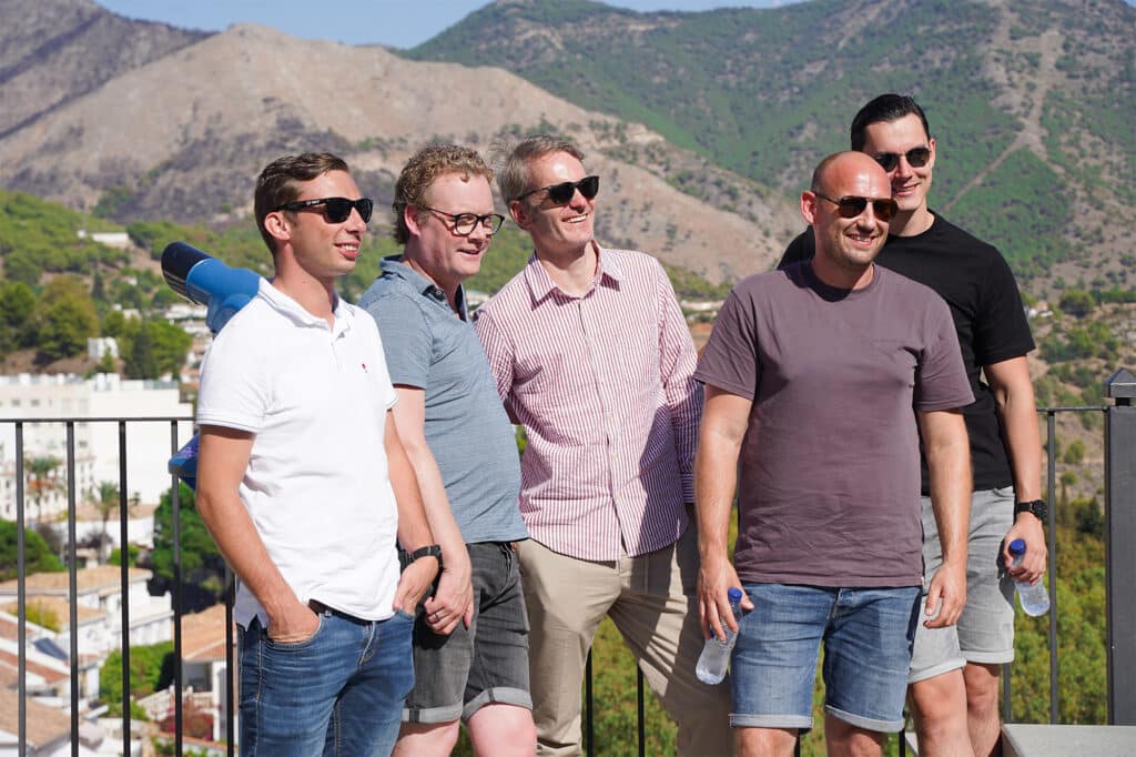 Publitas employees wearing sunglasses standing on a balcony. Sunny weather and a mountain behind them.