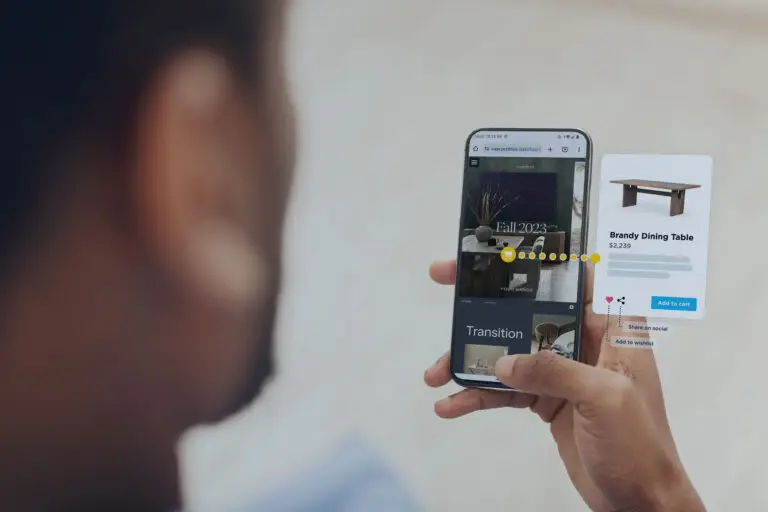 A man holding a phone showing a home deco digital catalog. A shopping cart icon and popup indicate that items from the catalog such as the Brandy Dining Table can be added to cart.