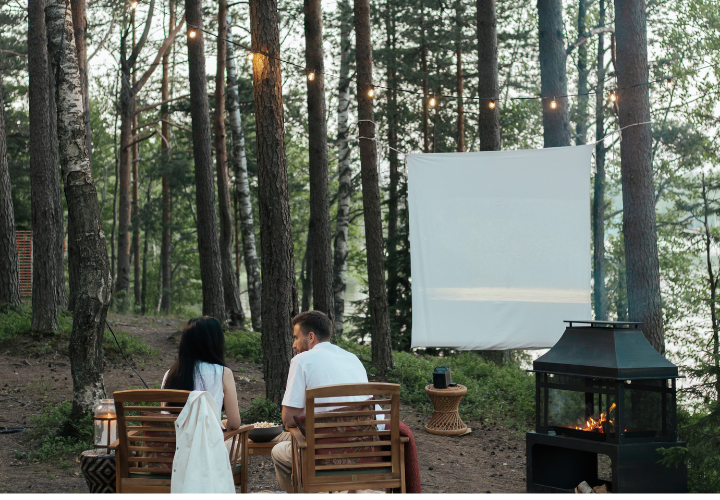 Why Supermarkets Need to Make Summer Retail Effortless 1 A man and a woman sitting in outdoor chairs in a forest in front of an outdoor movie screen