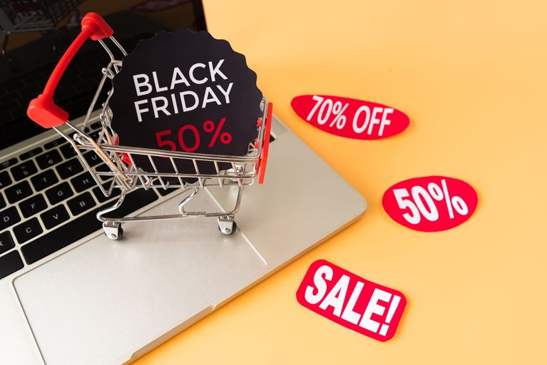 Miniature shopping cart on a laptop keyboard surrounded by Black Friday and sale stickers